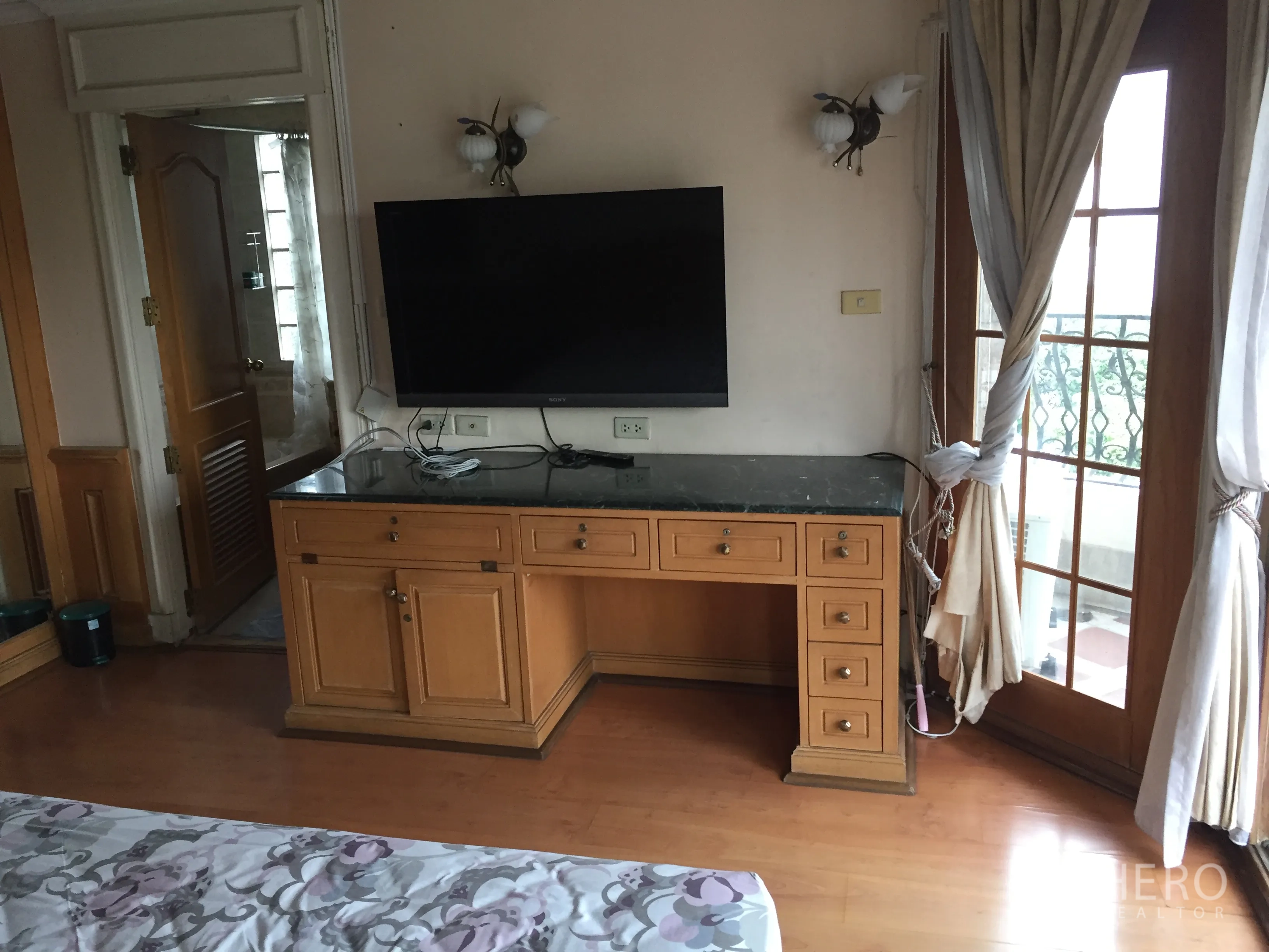 คอนโด ให้เช่าในKhlong Toei, Bangkok - ทีวีติดผนังเหนือโต๊ะทำงานไม้ ประตูบานฝรั่งเศสและผ้าม่านเปิดสู่ระเบียง