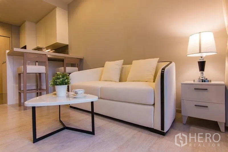 公寓 出售在Watthana, Bangkok - 明亮客厅，米色沙发、茶几与用餐吧台，色调柔和。