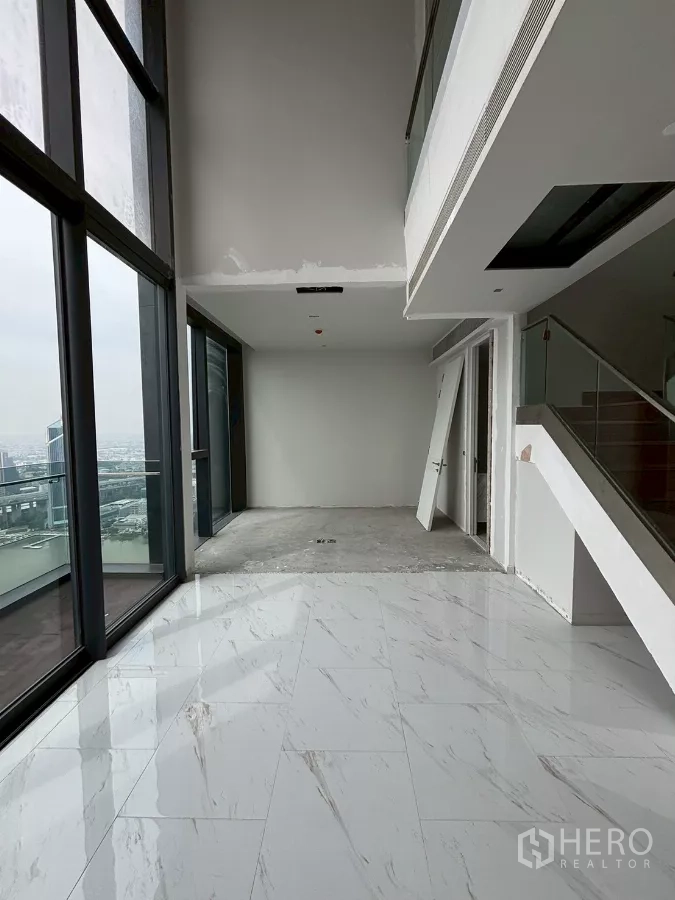 Condominium for sale in Bang Kho Laem, Bangkok - Double-height lounge with mezzanine and glass walls opening to a balcony.
