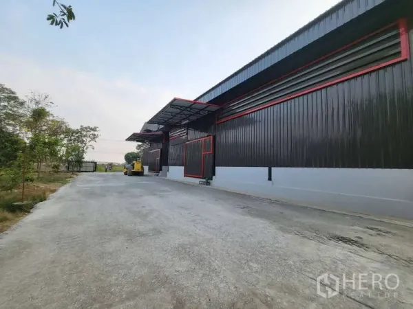 Warehouse for rent in Sam Phran, Nakhon Pathom - Side view of black metal-clad warehouse with loading canopies and a wide truck-friendly driveway.