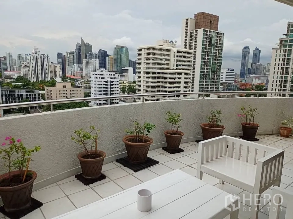 公寓 for rent in Watthana, Bangkok - 宽大阳台陈设白色户外家具与花盆，可欣赏无遮挡城市天际线。