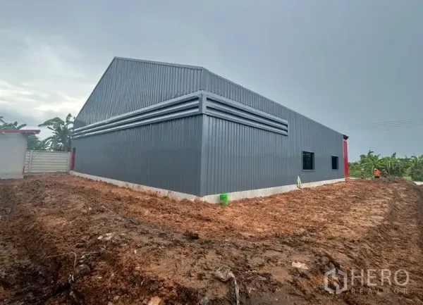 คลังสินค้า ให้เช่าในLam Luk Ka, Pathum Thani - มุมมองด้านข้างและด้านหลังของโกดังหลังคาทรงจั่ว มีแผงช่องลมและหน้าต่าง ล้อมรอบด้วยลานดินและกำแพงรั้ว