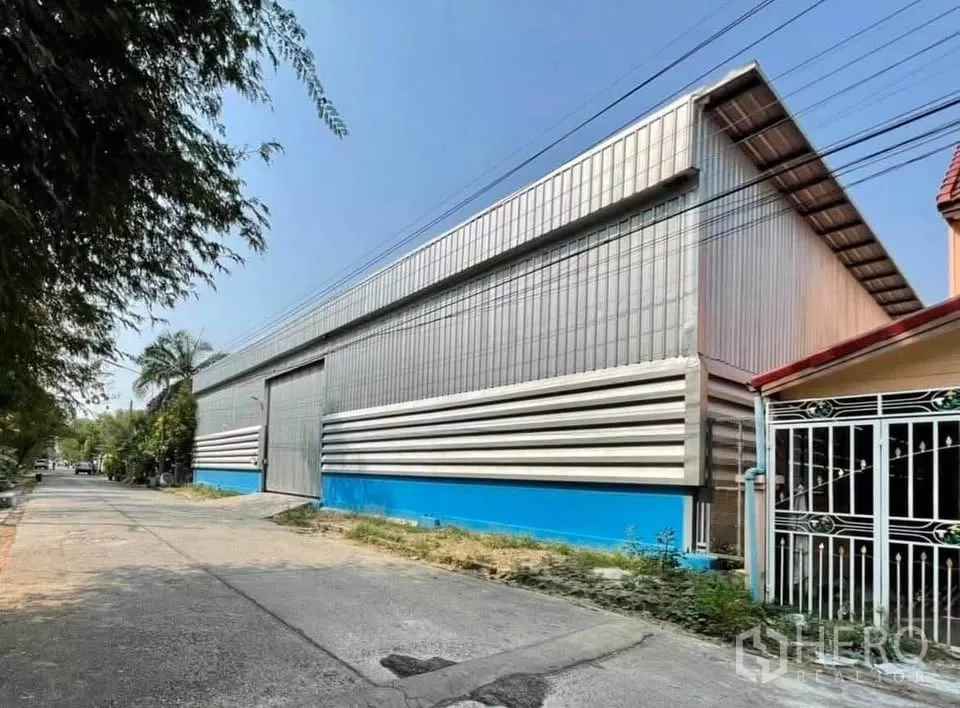 คลังสินค้า ให้เช่าในThanyaburi, Pathum Thani - มุมมองด้านหน้าโกดังโครงเหล็ก ผนังเมทัลชีท หลังคาสูง ประตูม้วนขนาดใหญ่ ในเขตธัญบุรี ปทุมธานี