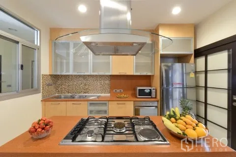 Apartment for rent in Watthana, Bangkok - Modern kitchen with gas cooktop island, range hood, mosaic backsplash, and stainless fridge.