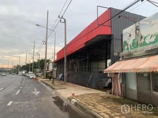คลังสินค้า ให้เช่าในBueng Kum, Bangkok - มุมด้านข้างของโกดังโครงเหล็กเพดานสูง แผ่นปิดสีแดง มีนั่งร้านอยู่ริมฟุตบาท.