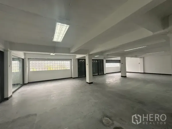 Office Space for rent in Khlong Toei, Bangkok - Wide office floor with concrete finish, pillars and a long glass-block wall.