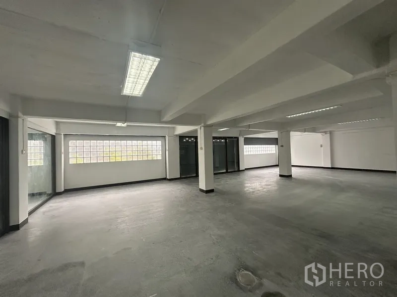 Office Space for rent in Khlong Toei, Bangkok - Wide office floor with concrete finish, pillars and a long glass-block wall.