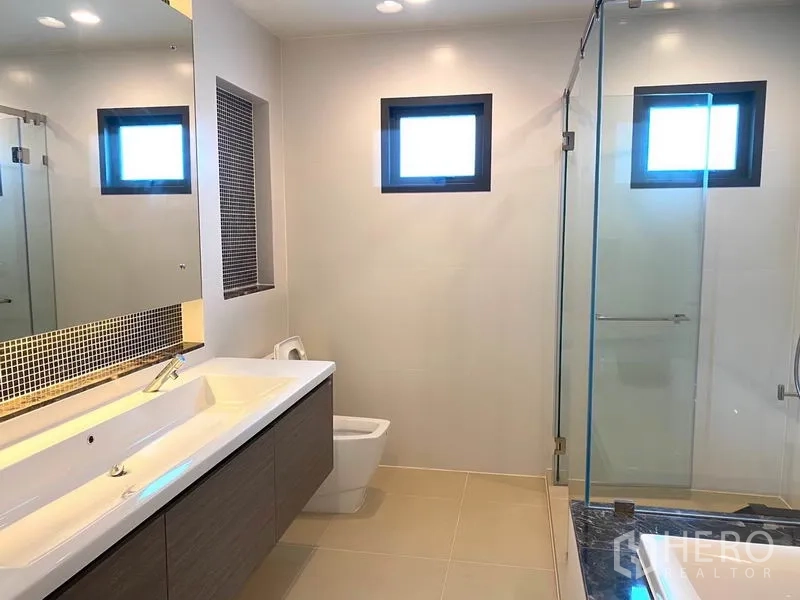 独立式住宅 出租在Saphan Sung, Bangkok - 浴室配长台面洗手池、大镜子、坐便器与玻璃淋浴间。