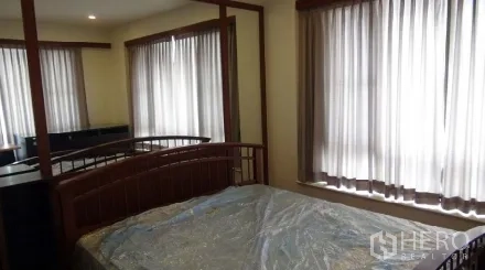 Condominium for rent or sale in Sathon, Bangkok - Second bedroom with corner windows, mirrored wardrobe, and wood bed frame.