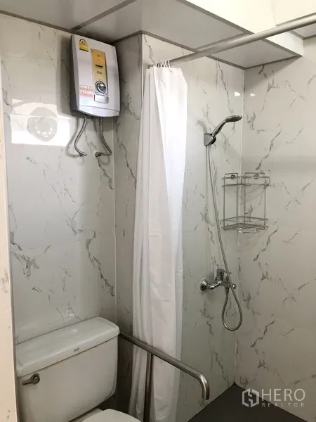 Apartment for rent in Suan Luang, Bangkok - Renovated bathroom with marble‑look tiles, shower with curtain, water heater and a safety grab bar.