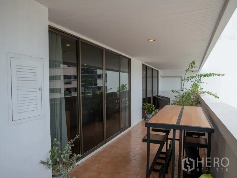 Apartment for rent in Khlong Toei, Bangkok - Long balcony with high table and stools facing sliding glass doors.