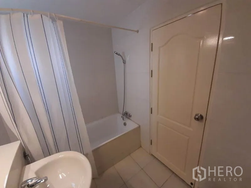 Condominium for sale in Wang Thonglang, Bangkok - Bathroom with bathtub, shower and striped curtain in Bangkok condo.