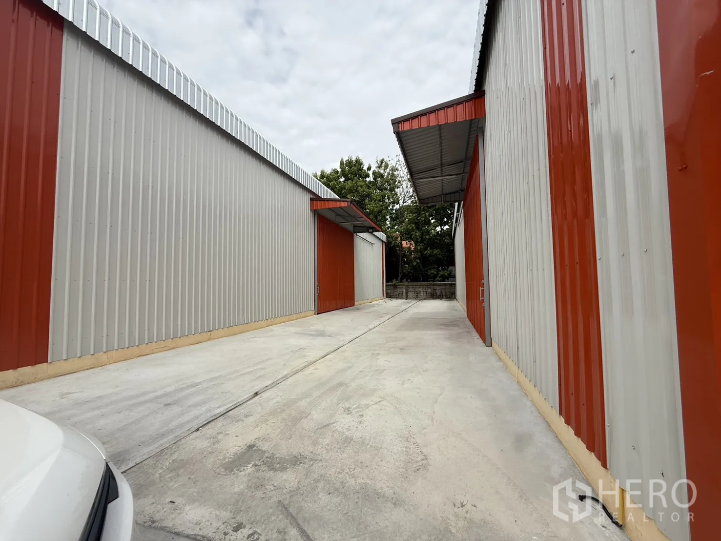Warehouse for rent in Wang Thonglang, Bangkok - Side driveway between warehouse buildings with canopies and a boundary wall.