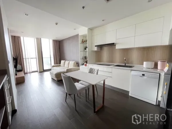 Condominium for rent in Pathum Wan, Bangkok - Open-plan living area with white kitchen, dining table, and floor-to-ceiling windows.