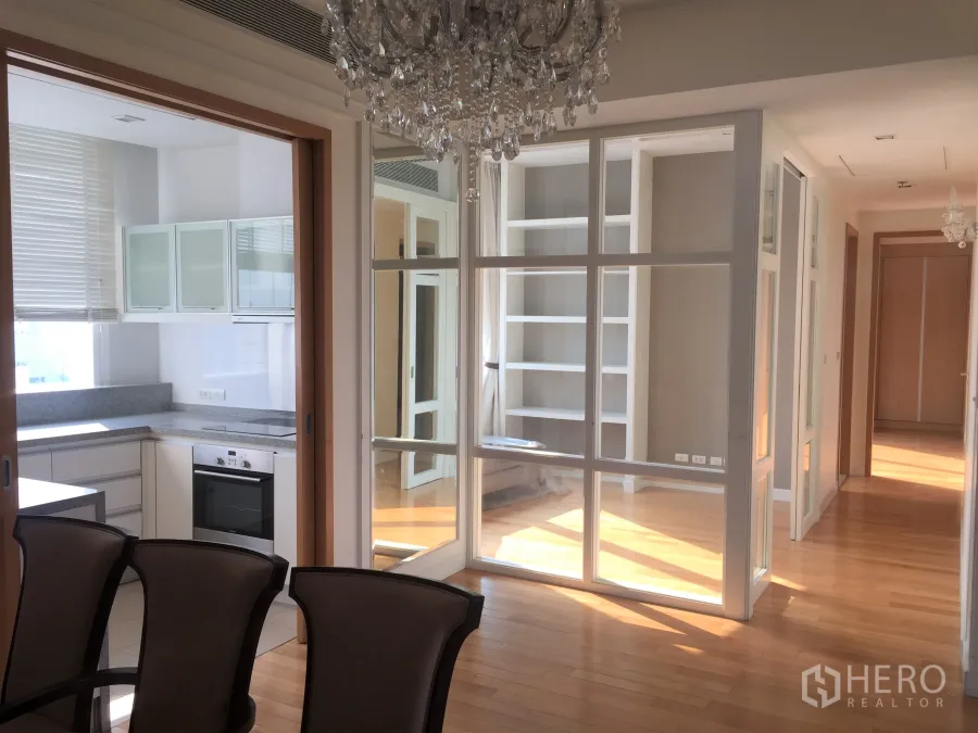 คอนโด ให้เช่าในKhlong Toei, Bangkok - พื้นที่รับประทานอาหารสว่างพร้อมโคมระย้า ผนังกระจกกั้นห้อง และทางเข้าครัวปิดบนพื้นไม้