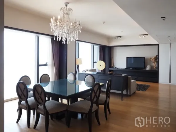 Condominium for rent in Sathon, Bangkok - Open-plan living and dining area with a crystal chandelier, glass table and floor-to-ceiling windows in a Sathon condo.