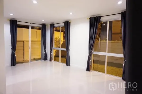 สำนักงานที่บ้าน ให้เช่าหรือขายในBang Khen, Bangkok - ห้องนั่งเล่นชั้นล่างสว่าง พื้นกระเบื้องเงา ไฟดาวน์ไลท์ และหน้าต่างบานใหญ่พร้อมผ้าม่านทึบ