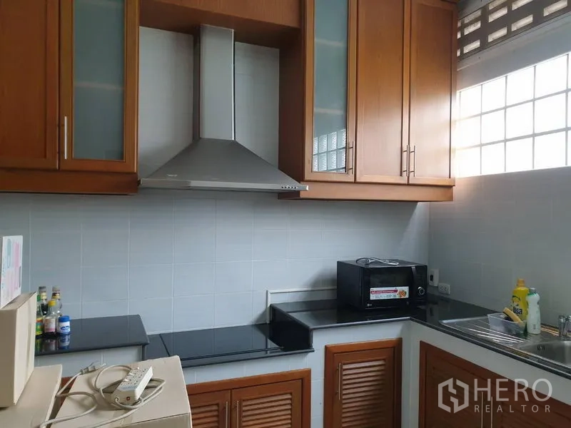 Townhouse for rent in Bang Kho Laem, Bangkok - U-shaped kitchen with wooden cabinets, range hood, glass-block window and black countertops.