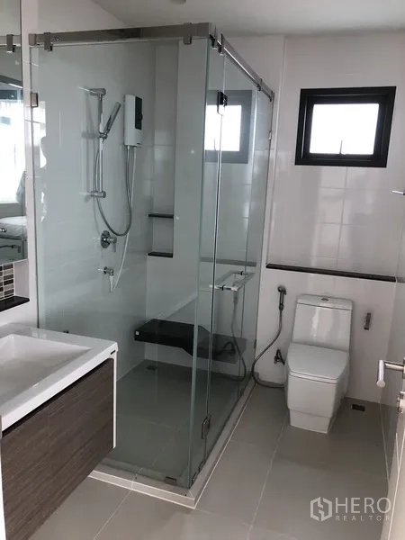 Detached House for rent in Bang Kapi, Bangkok - Contemporary bathroom with glass-enclosed shower, vanity, and a window for ventilation.