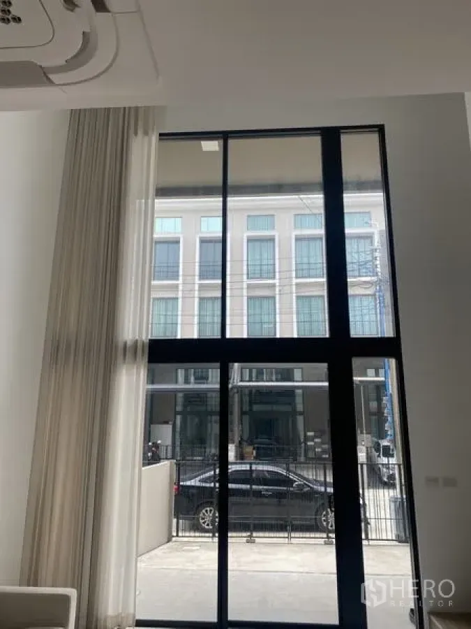Townhouse for rent or sale in Bang Khae, Bangkok - Bright living area with double-height black-framed windows facing the street