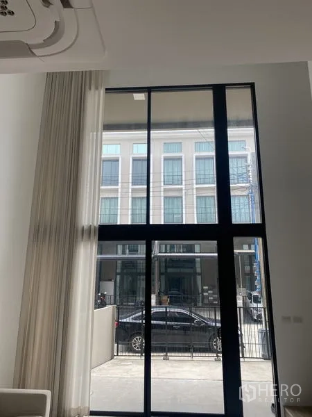 Townhouse for rent or sale in Bang Khae, Bangkok - Bright living area with double-height black-framed windows facing the street