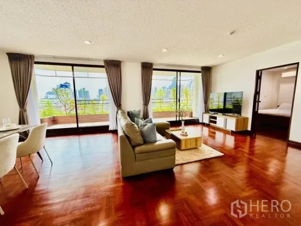 Condominium for rent - Spacious living room with sofa and TV facing wide glass doors to a balcony with green planters.