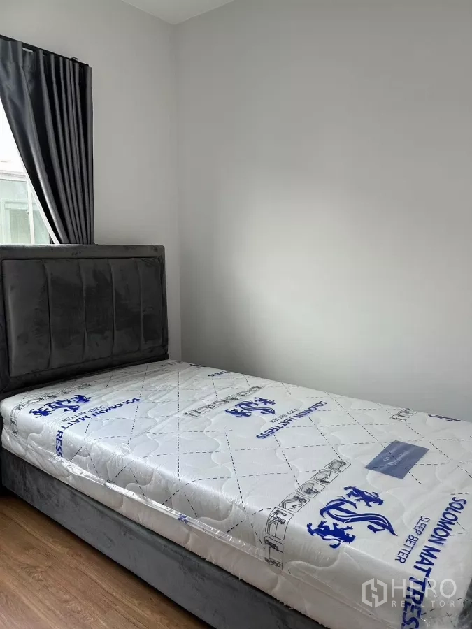 Townhouse for rent in Bang Phli, Samut Prakan - Cozy single bedroom with grey upholstered bed and window curtains.