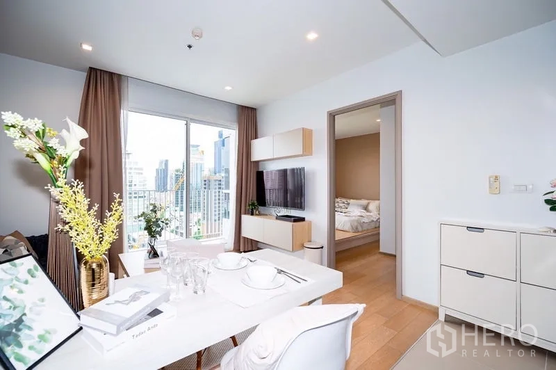 Condominium for rent or sale in Watthana, Bangkok - Dining table facing TV wall with sliding door to the bedroom and floor-to-ceiling windows overlooking the skyline.