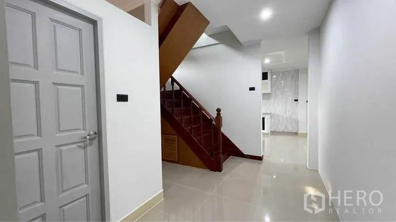 Detached House for rent in Bang Kapi, Bangkok - Hallway with wooden staircase and glossy floor tiles connecting toward the kitchen.