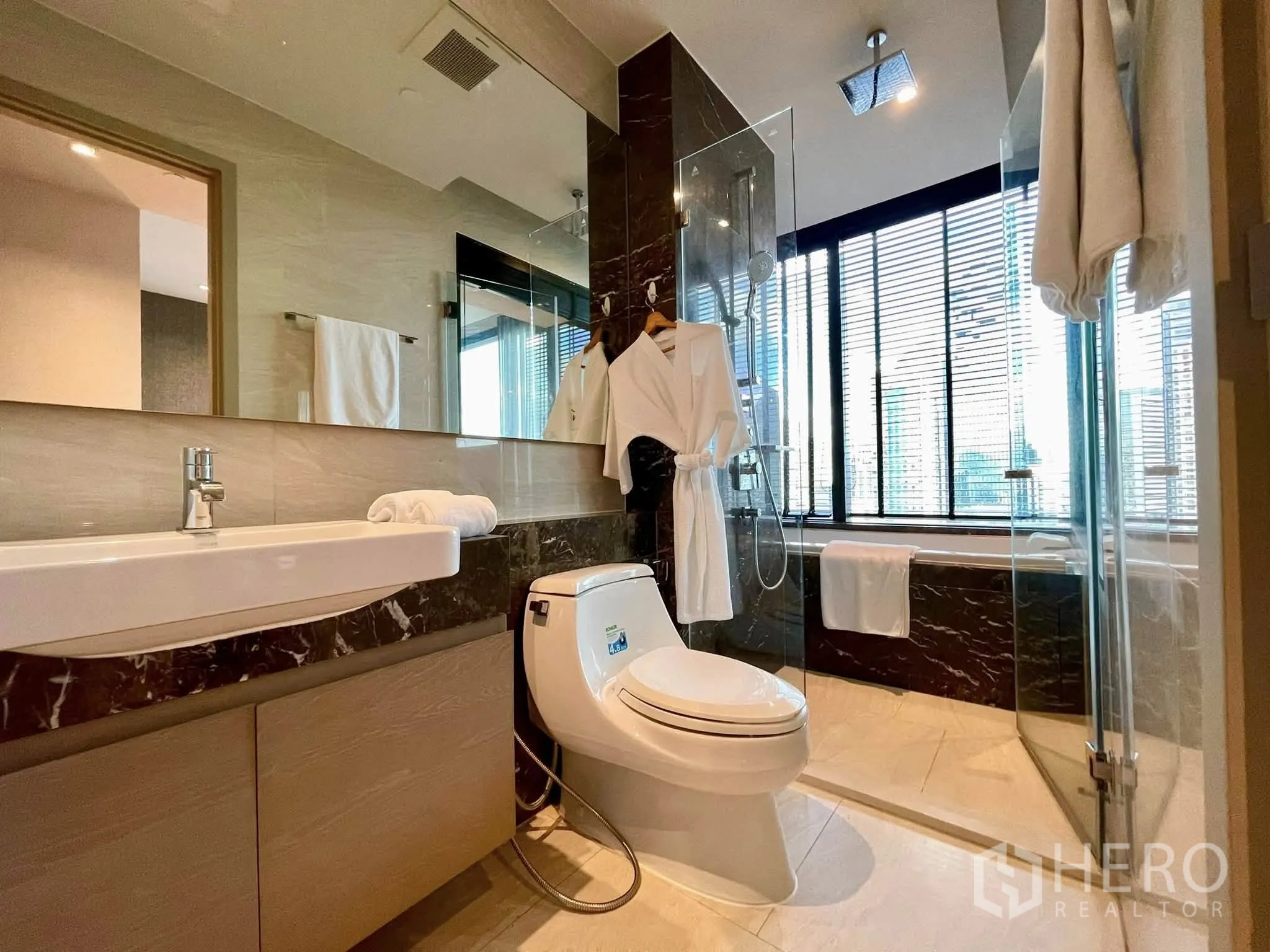 Condominium for rent in Bang Rak, Bangkok - Bathroom with glass shower, bathtub, long mirror and window blinds.