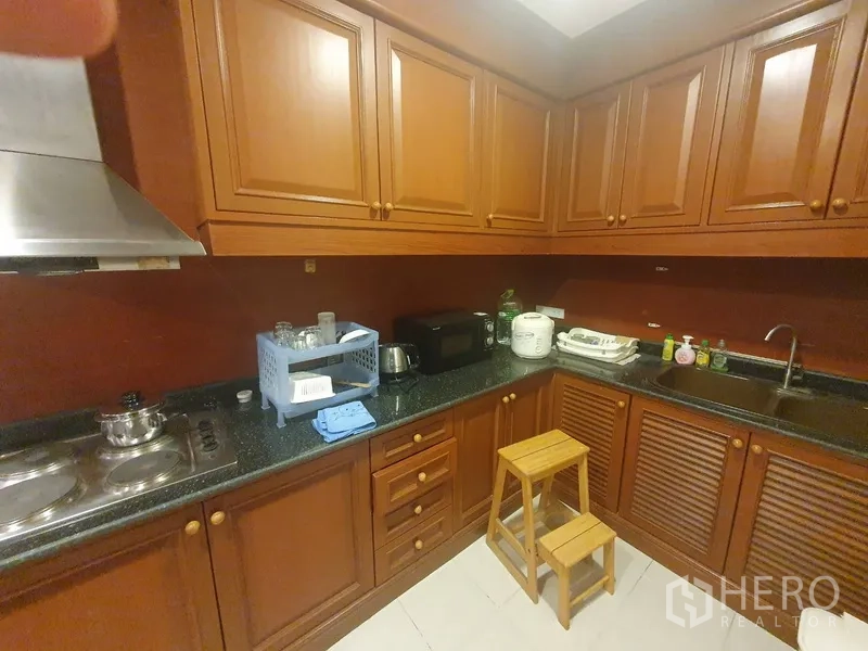 Condominium for rent in Bang Kho Laem, Bangkok - Closed kitchen with wood cabinetry, black stone countertops, cooktop and stainless range hood.
