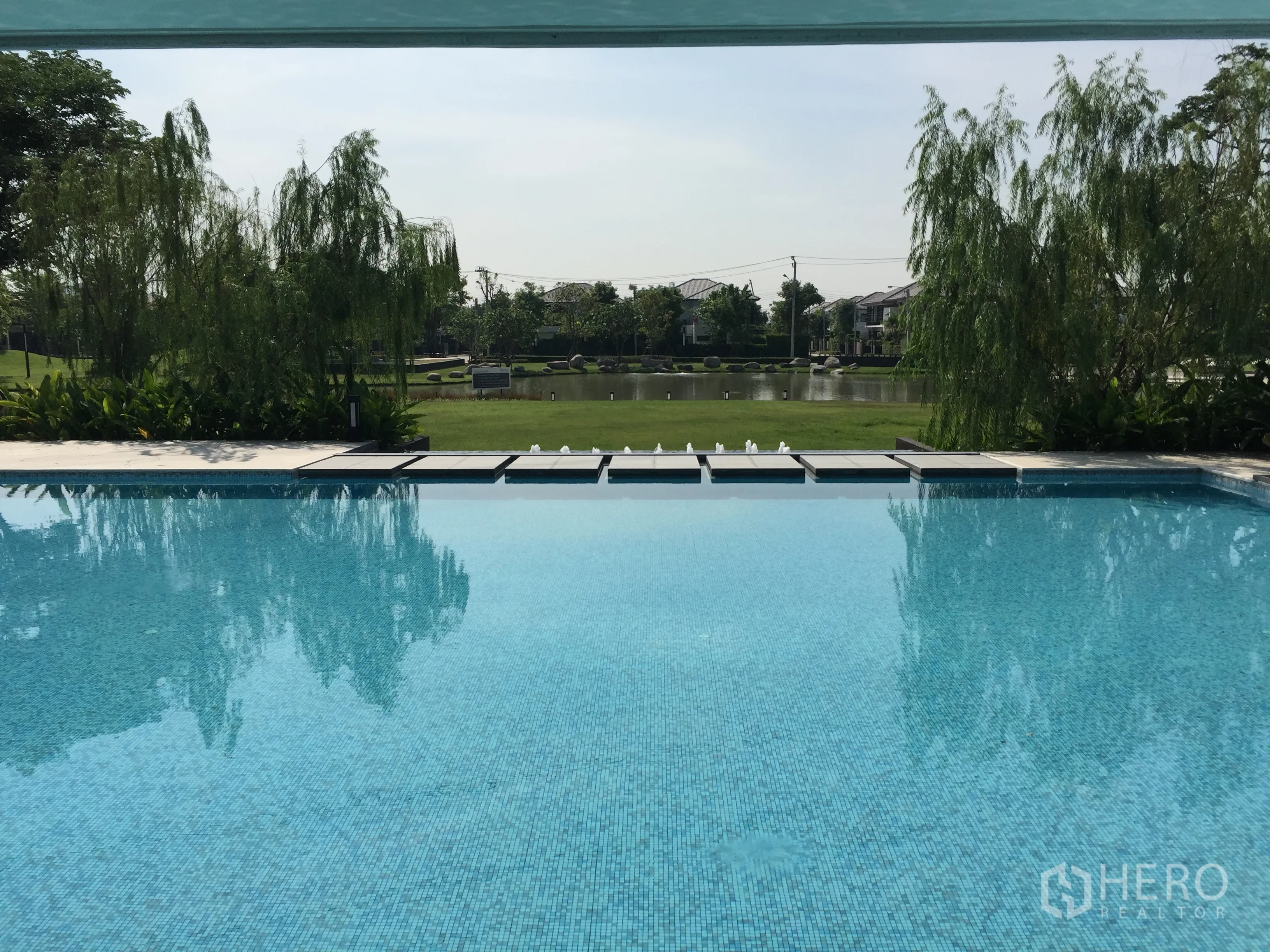Detached House for rent or sale in Prawet, Bangkok - Community swimming pool overlooking a landscaped lake and greenery within the estate.