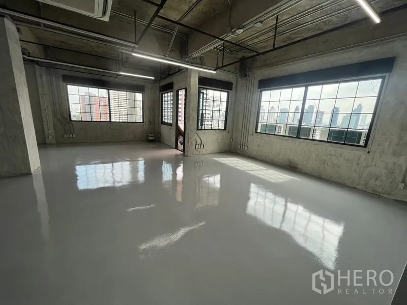 Office Space for rent in Khlong Toei, Bangkok - Loft-style open-plan office with polished epoxy flooring, exposed concrete ceiling, black-framed windows and skyline views.