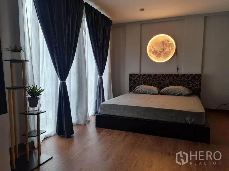 Townhouse for sale in Suan Luang, Bangkok - Master bedroom with large windows, dark curtains and a moon-inspired wall light.