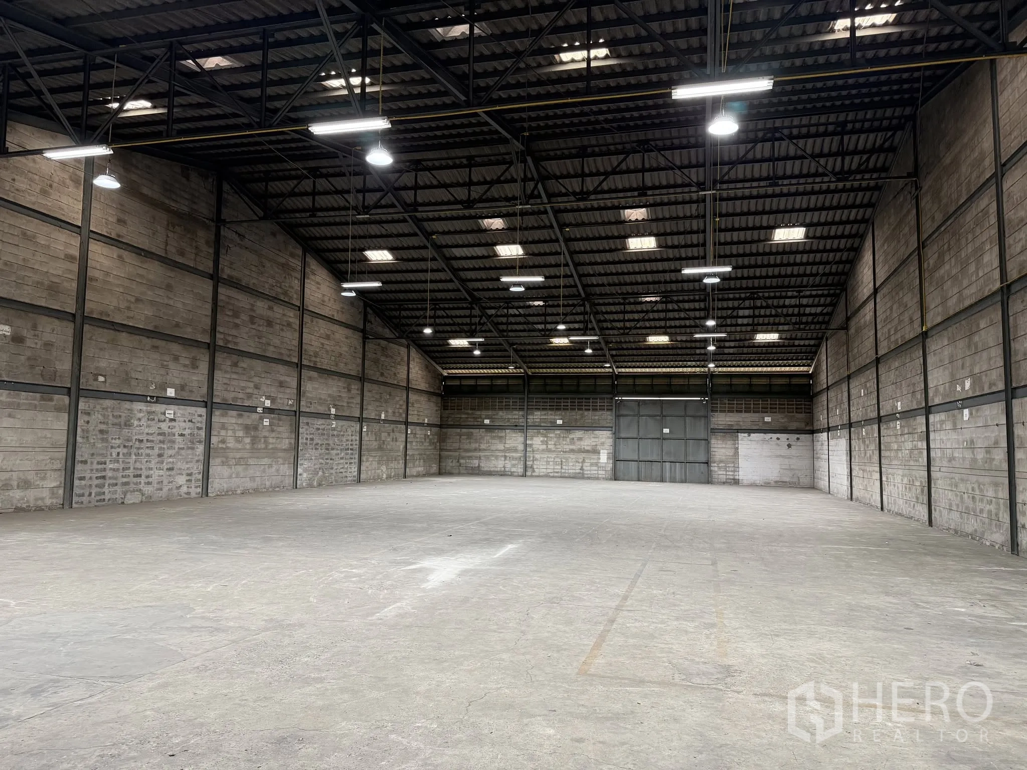 Warehouse for rent in Bang Na, Bangkok - Wide warehouse interior with high ceiling, steel trusses, concrete floor, and large loading doors.