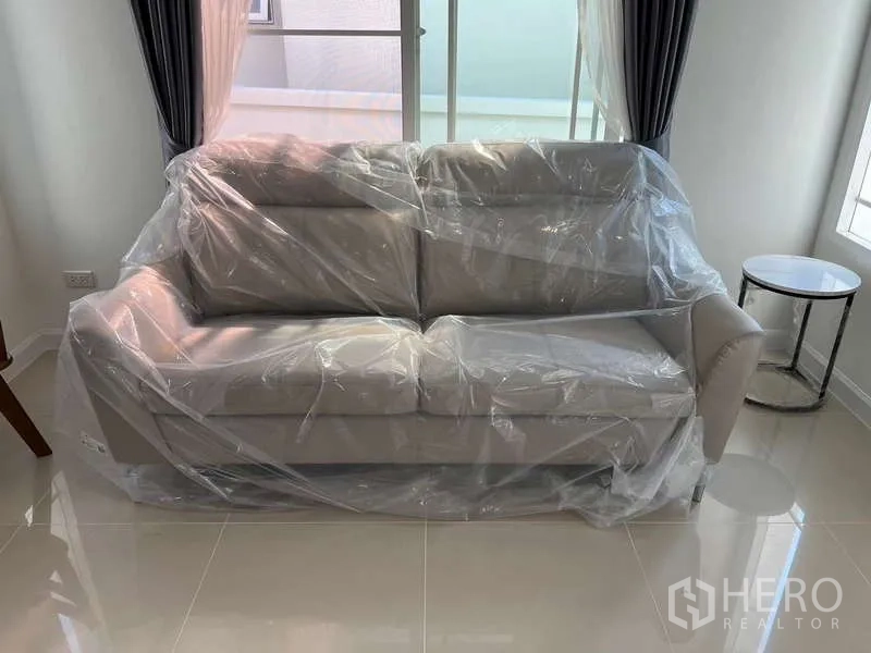 บ้าน ให้เช่าในBang Kapi, Bangkok - โซฟาสีเทาใหม่หุ้มพลาสติกในห้องนั่งเล่นพื้นกระเบื้องสว่าง