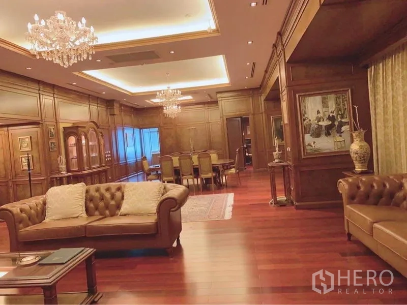Condominium for rent in Watthana, Bangkok - Grand living and dining room with rich wood paneling, coffered ceilings, chandeliers, and leather sofas on polished hardwood floors.