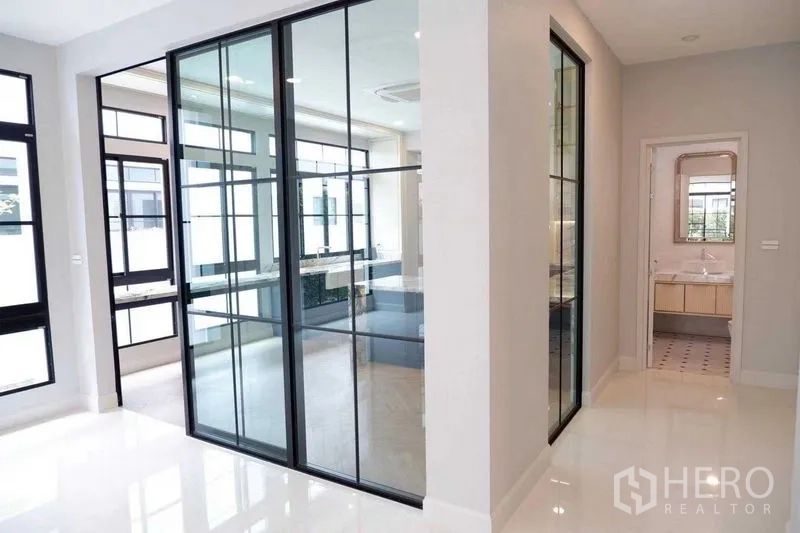 Detached House for sale in Saphan Sung, Bangkok - Hallway with black-framed glass partitions and view toward a bathroom.