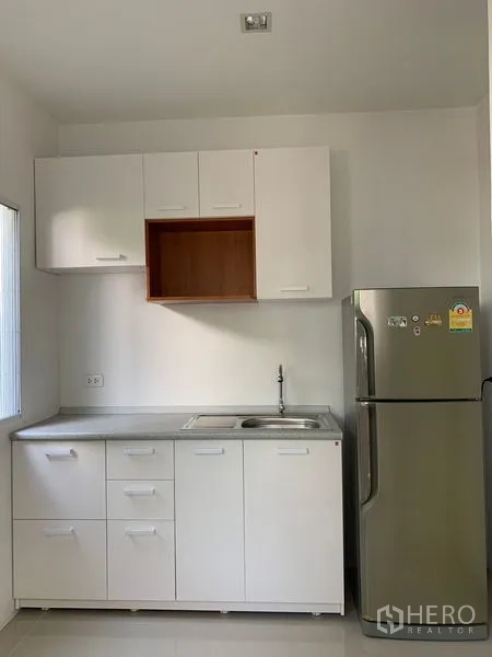 Detached House for sale in Prawet, Bangkok - Minimal white kitchen with cabinets, sink and stainless refrigerator.