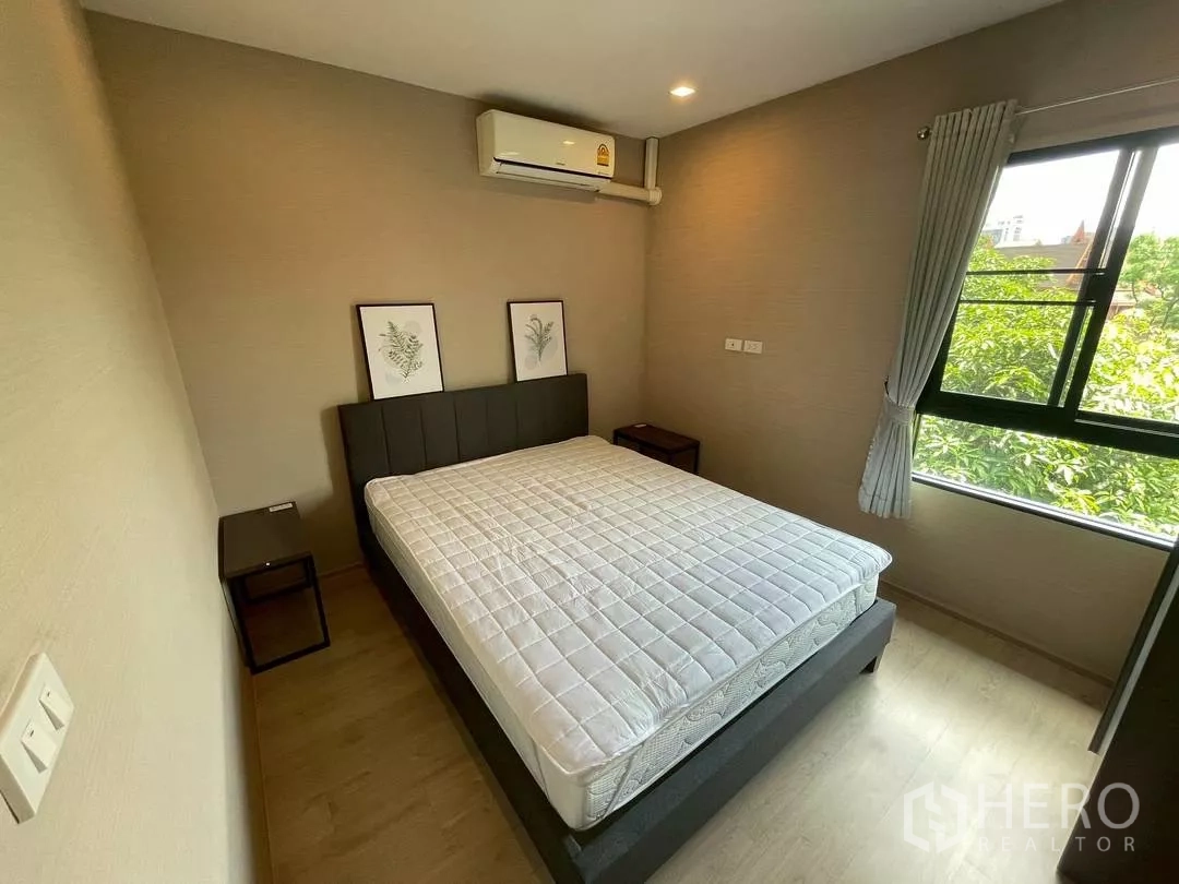 ทาวน์เฮาส์ ให้เช่าในSuan Luang, Bangkok - ห้องนอนสว่างด้วยหน้าต่างบานใหญ่ มีเครื่องปรับอากาศ และภาพตกแต่งลายใบไม้เหนือโต๊ะข้างเตียง.