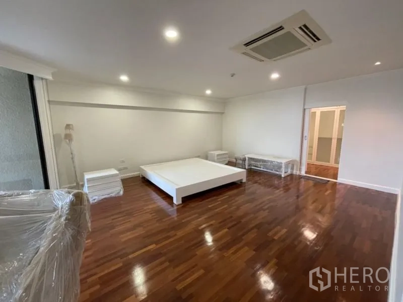 คอนโด ให้เช่าในKhlong Toei, Bangkok - ห้องนอนใหญ่ พื้นไม้ เตียงแพลตฟอร์ม และทางออกสู่ระเบียงผ่านประตูกระจก