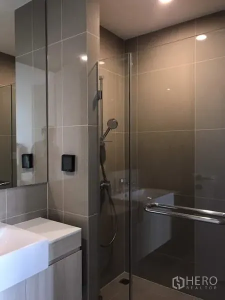 Condominium for rent or sale in Watthana, Bangkok - Modern bathroom with full‑height tiles, glass shower enclosure, handheld shower, and square vanity sink.