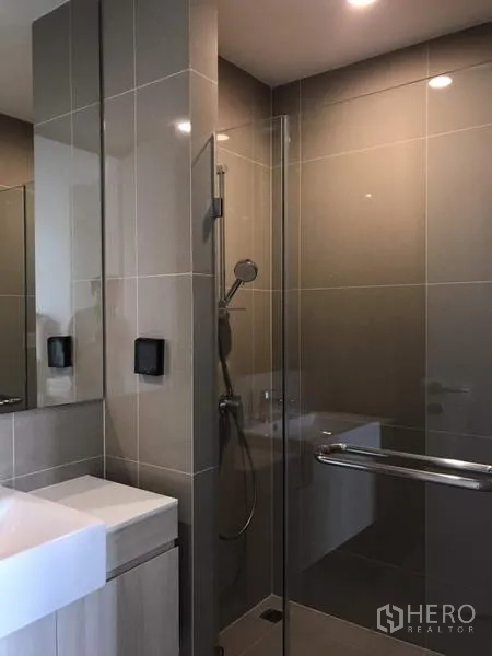 Condominium for rent or sale in Watthana, Bangkok - Modern bathroom with full‑height tiles, glass shower enclosure, handheld shower, and square vanity sink.