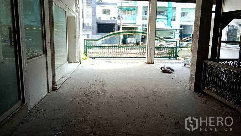 Warehouse for rent in Nakhon Pathom - Covered loading and entry area facing a gated entrance and neighboring buildings.