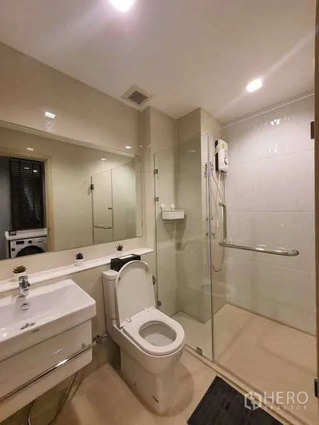 Condominium for rent - Bathroom with vanity, large mirror, toilet, and walk-in shower behind glass screen.