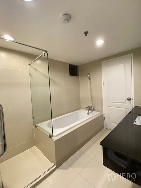 Condominium for rent - Bathroom featuring bathtub with glass screen and long vanity counter.