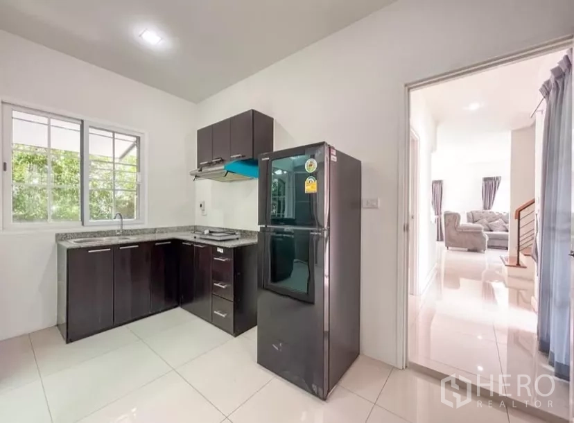 独立式住宅 出租在Chom Thong, Bangkok - 厨房带双门冰箱与抽油烟机，连接明亮客厅视野。