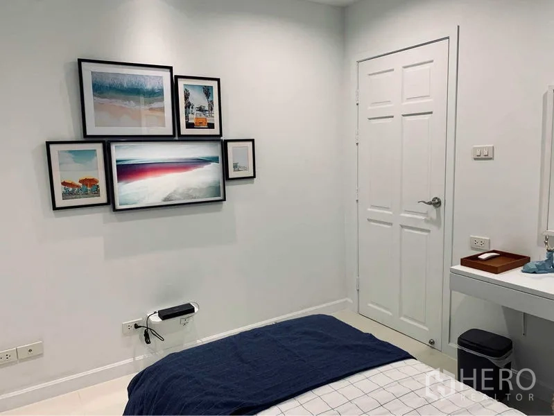 คอนโด ให้เช่าในWatthana, Bangkok - ผนังห้องนอนมินิมอลประดับกรอบรูปหลายชิ้น เหนือเตียงและประตูสีขาว