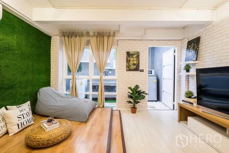 บ้าน ให้เช่าในKhlong Toei, Bangkok - มุมนั่งเล่นยกระดับ พื้นไม้ ผนังหญ้าเทียม และชั้นวางทีวี