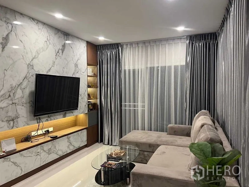 บ้าน ให้เช่าหรือขายในLat Krabang, Bangkok - ห้องนั่งเล่นผนังลายหินอ่อน ทีวีติดผนัง โซฟาเข้ามุม ผ้าม่านโปร่งและไฟดาวน์ไลท์